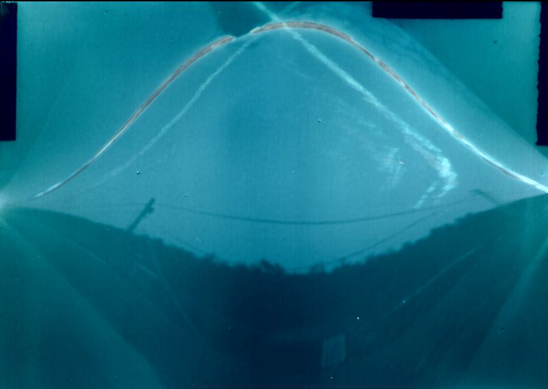 Cyanotype-toned solargraph aimed north with about 45 degree tilt showing a broad Sun arc over a bowl-shaped horizon silhouette